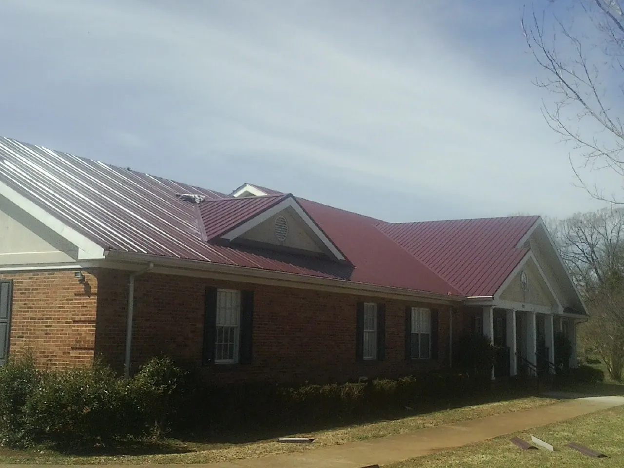 Red metal roof with gabled entries on a long brick building, from a Hail Damage Roof Repair job in Travelers Rest