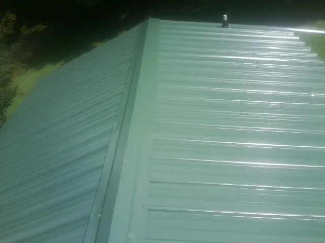 New green metal panels meeting at the ridge of a roof — Flat Roof Repair work by our crew in Travelers Rest