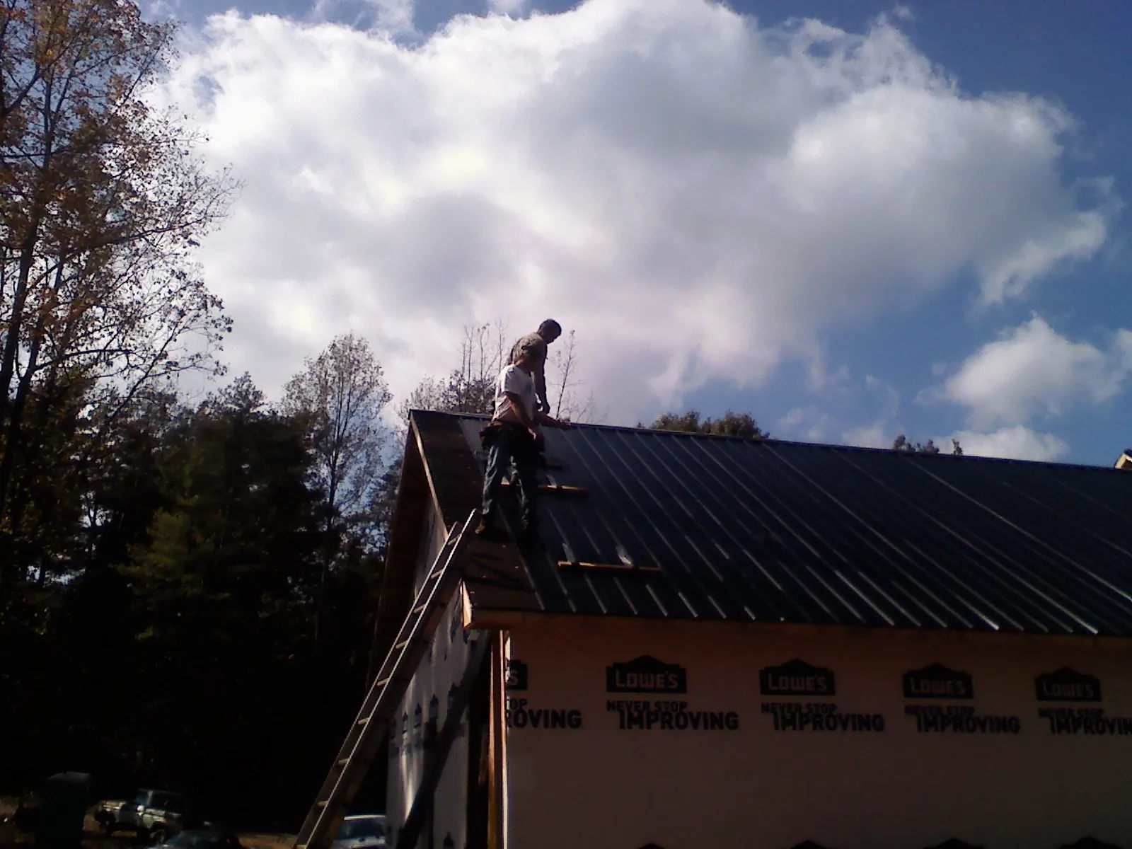 Roofer fastening dark metal panels high against a cloudy sky, from a Roof Inspection job in Travelers Rest