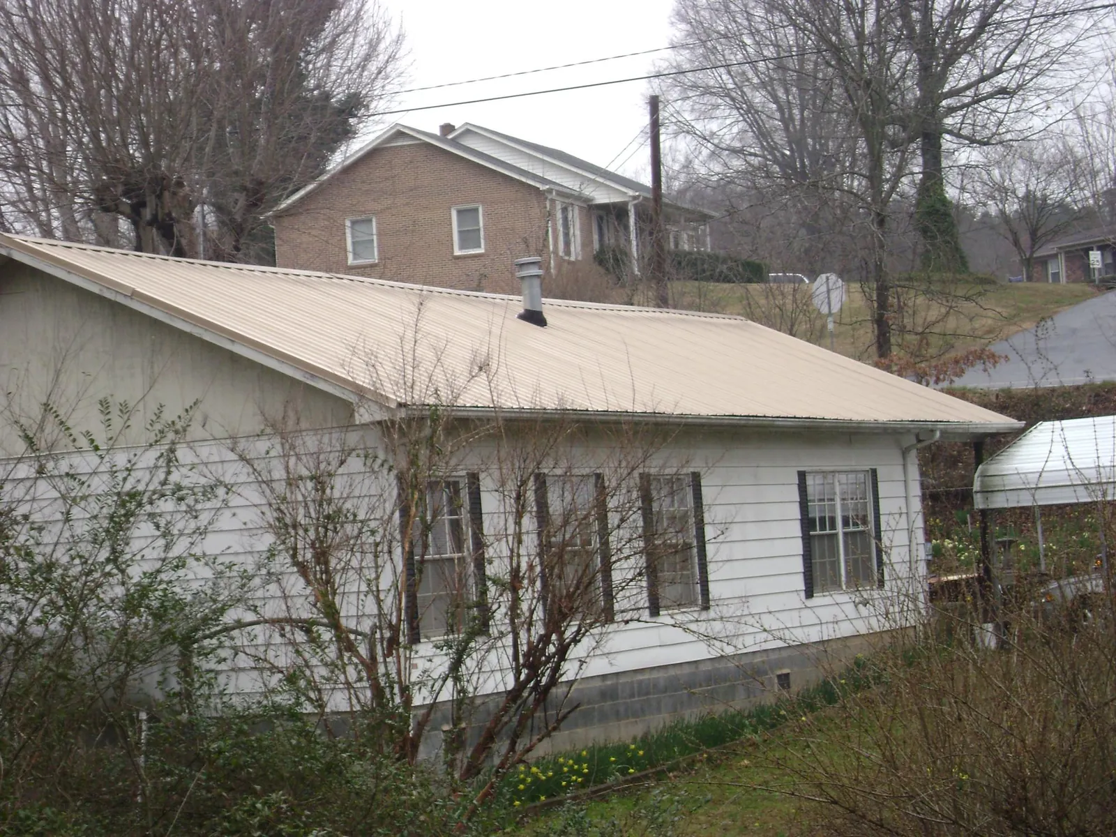 Tan metal roof on a white sided house set into a hillside — Commercial Roofing by Roofing Brothers in Travelers Rest
