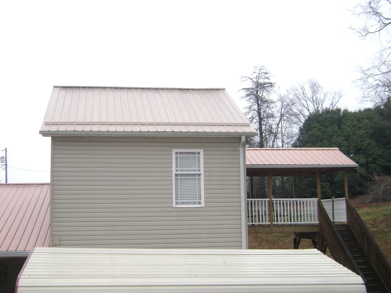 Tan metal roofs on a two story addition and attached porch, from a Roof Replacement job in Travelers Rest